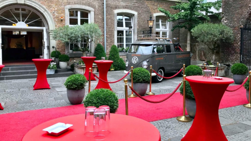 Exklusive Outdoor-Eventlocation mit rotem Teppich, Stehtischen und Vintage-VW-Bus.