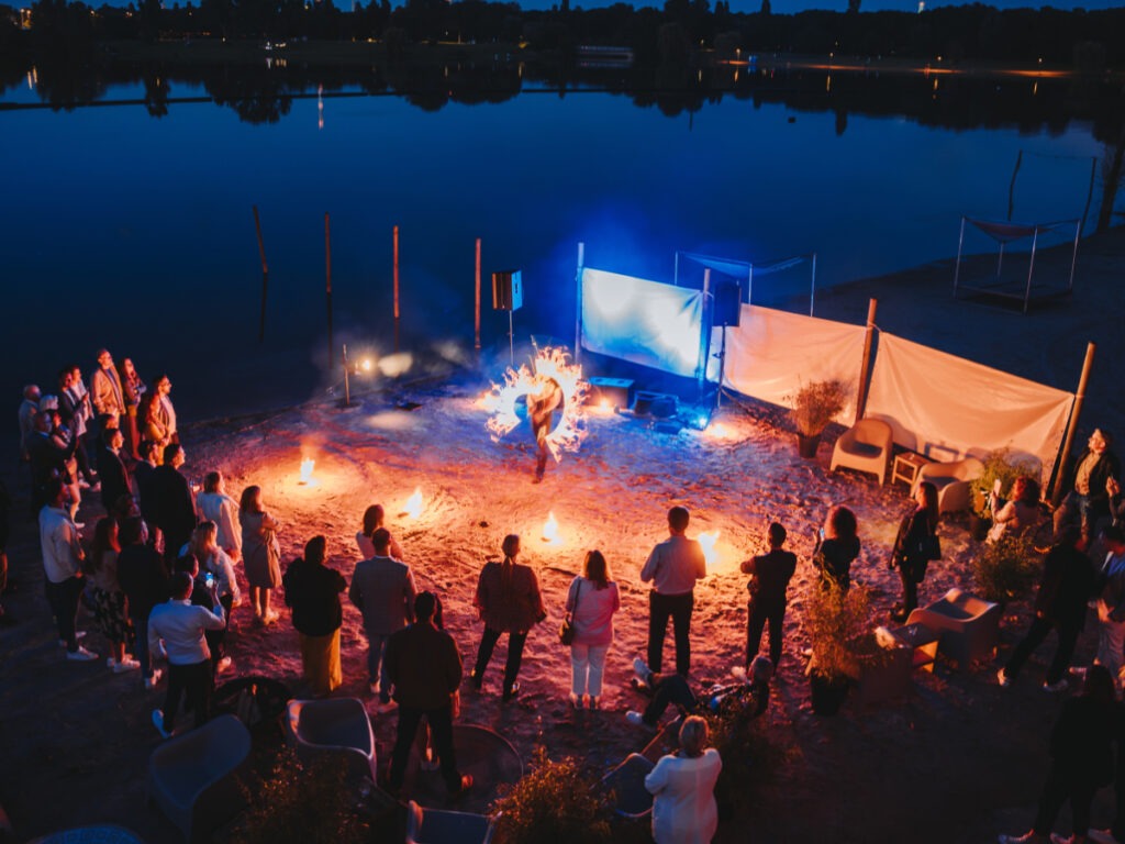 Feuershow am See bei Nacht mit begeistertem Publikum und stimmungsvoller Beleuchtung.