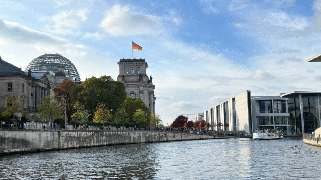 Reichstagsgebäude mit Glaskuppel und Spree im Vordergrund, flankiert vom modernen Regierungsviertel in Berlin.