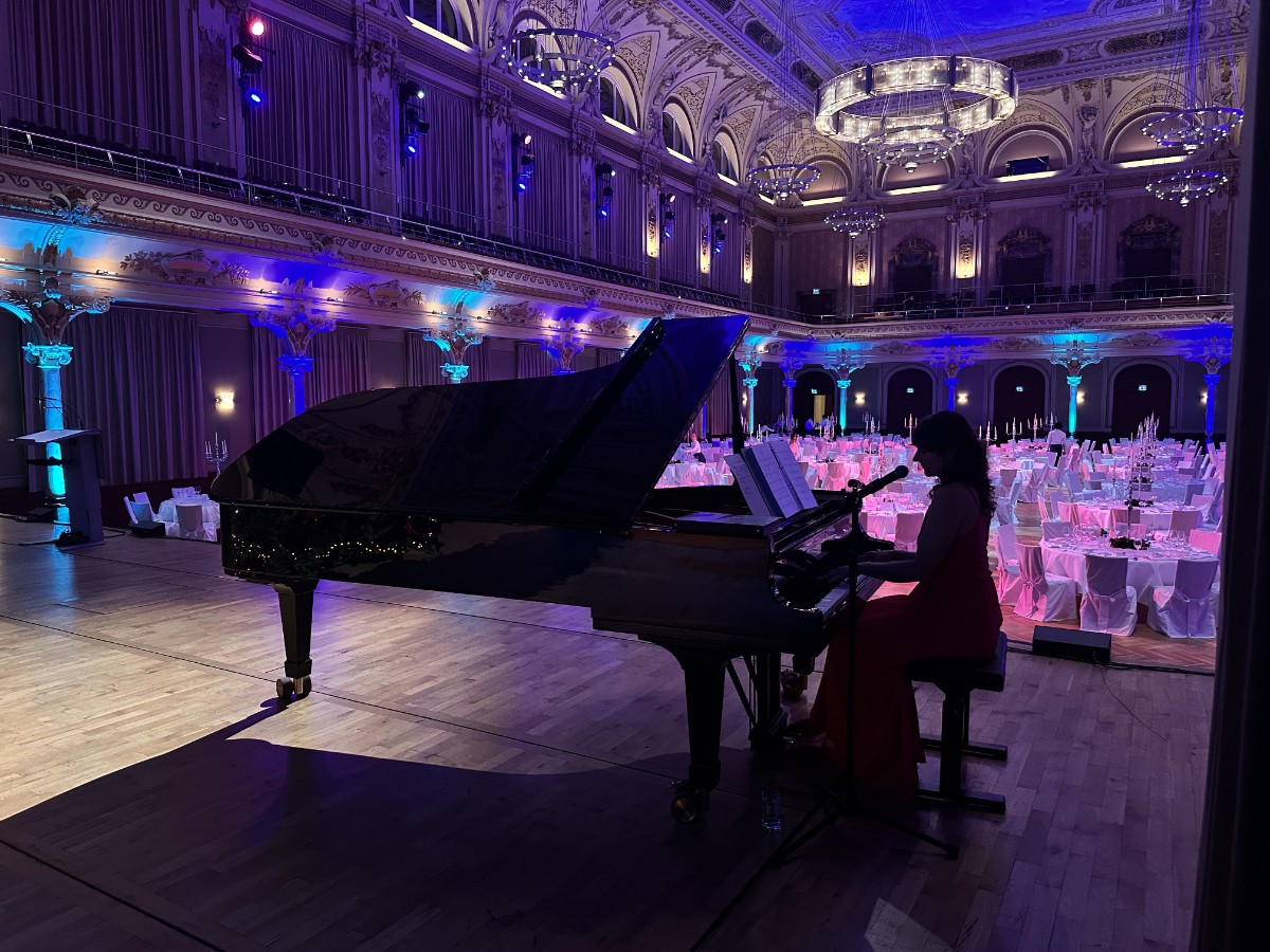 Zuzanna Kies am Konzertflügel in einem prachtvoll ausgeleuchteten Ballsaal während eines exklusiven Dinners.