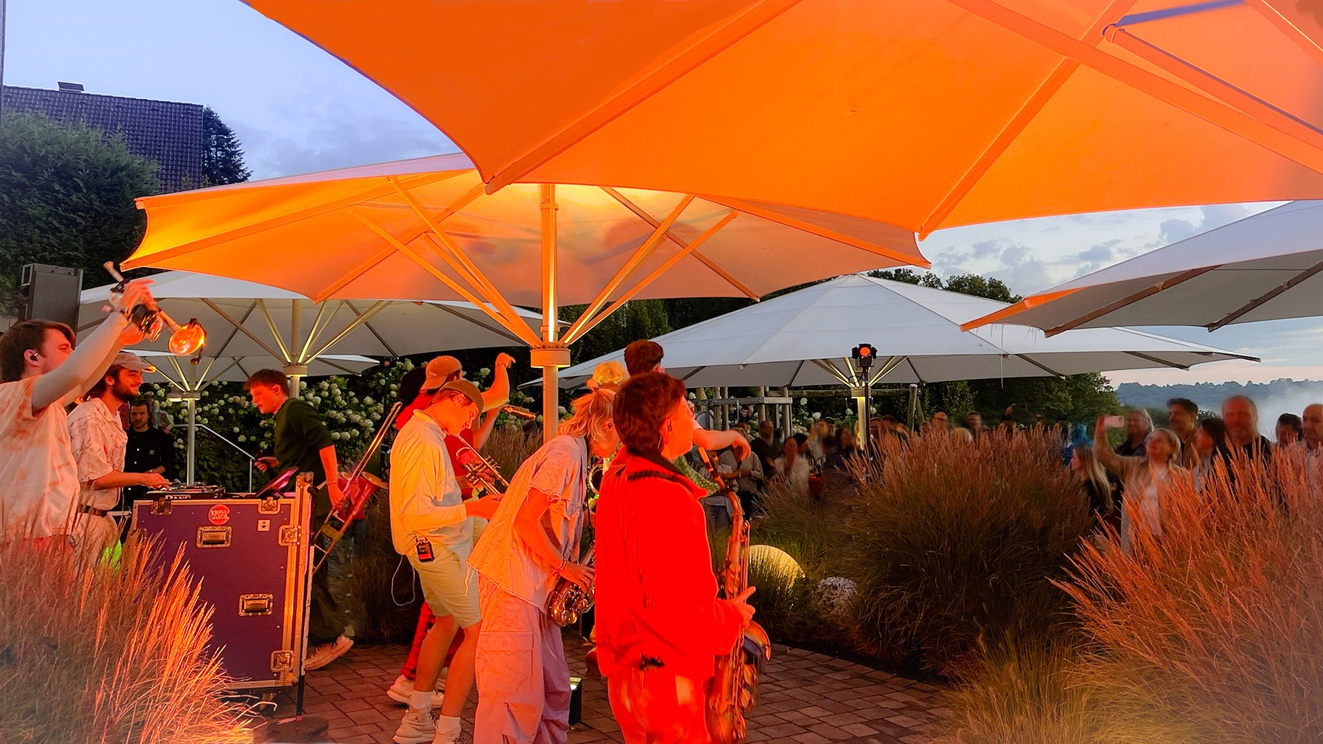 Live-Band spielt auf einem Outdoor-Firmenevent unter orangefarbenen Sonnenschirmen. Professionelles Business-Event der Kölner Eventagentur Menschen Emotionen Erlebnisse.